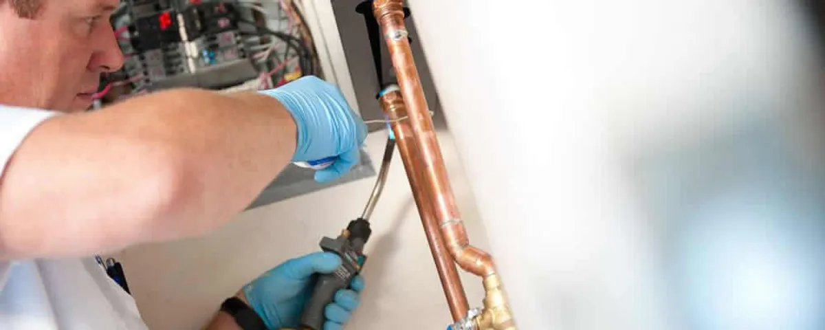 Water heater repair technician testing copper pipe connections and controls in Houston, TX